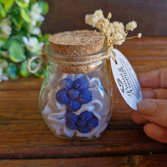 Vela decorativa aromática con flores en recipiente de vidrio con tapa de corcho