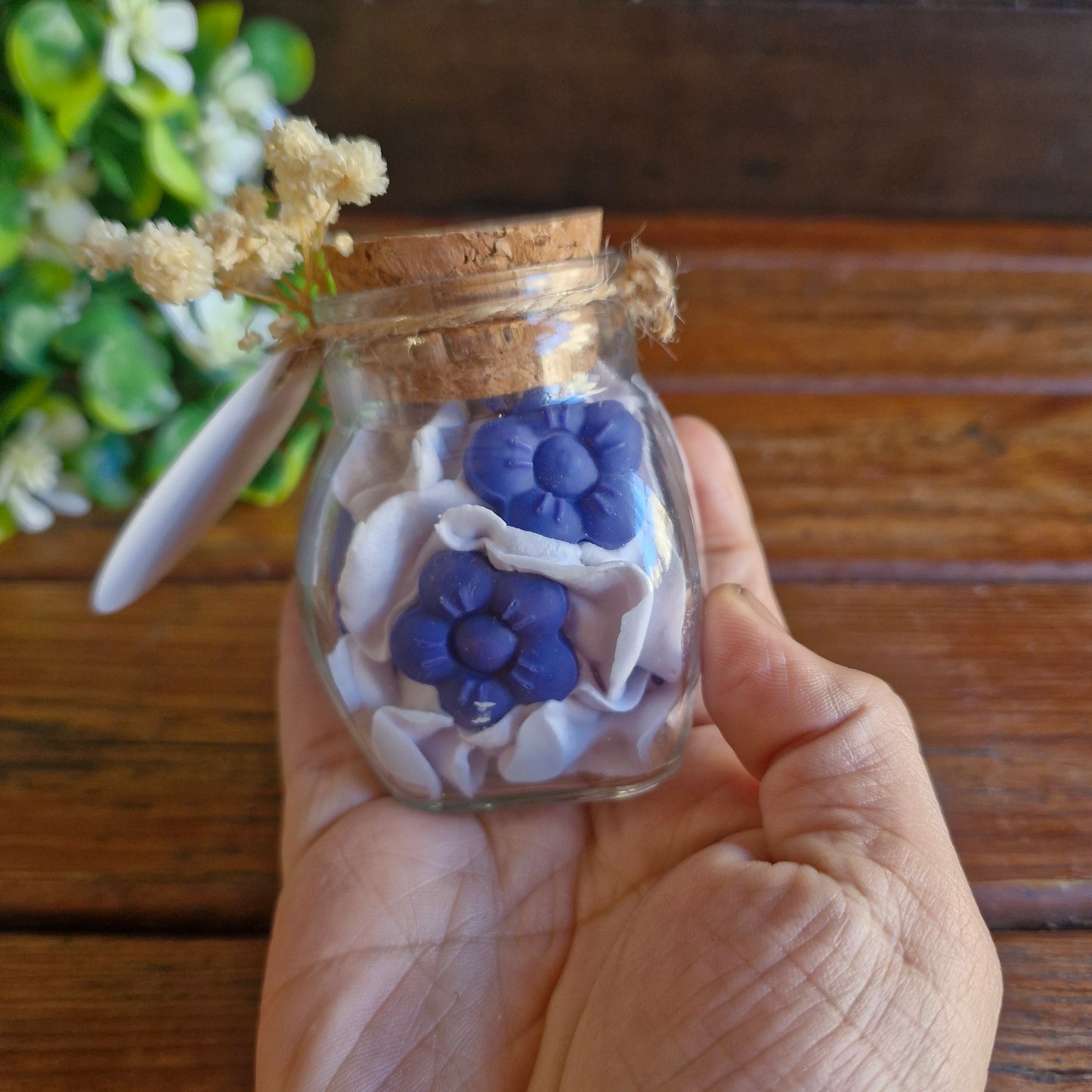 Vela decorativa aromática con flores en recipiente de vidrio con tapa de corcho